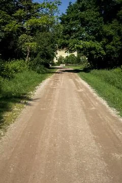 Path bordered by trees in a park that leads to a mansion on a sunny day in .. Stock Photos