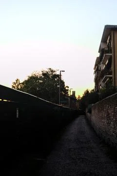 Path bordered by a wall and a fence in a residential area at sunset Stock Photos