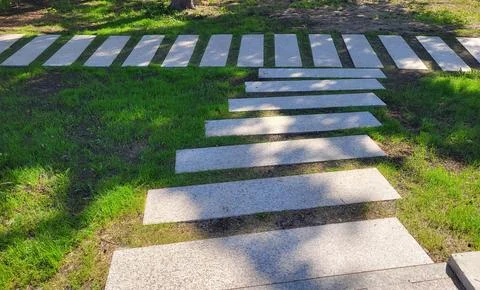 A path of concrete rectangles is laid across the shady spring green lawn. The 스톡 사진
