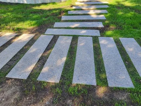 A path of concrete rectangles is laid across the spring green lawn. The con.. 스톡 사진