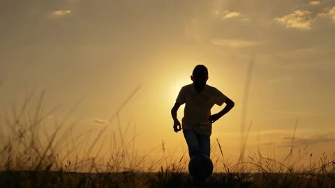The path to the dream. The silhouette of a child chasing a ball with his foot at Stock-Footage 136283069