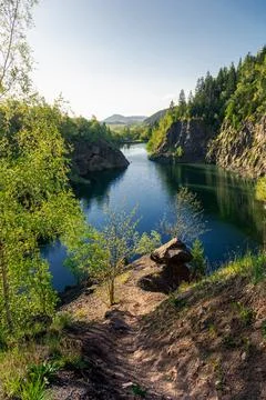 Path leading to a big boulder over quarry filled with water Stock Photos