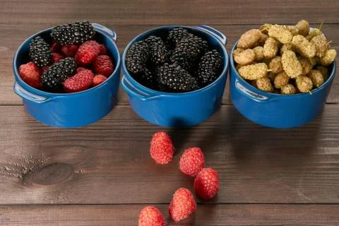 Path made from raspberries to three small ceramic bowl full of berries Stock Photos