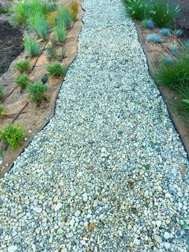 Path made of small stones and grass borders in a garden setting during daylig Stock Photos