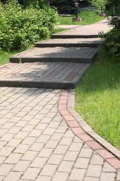 Path with steps in park made of tiles. Green trees and bushes in summer on sunny Stock Photos