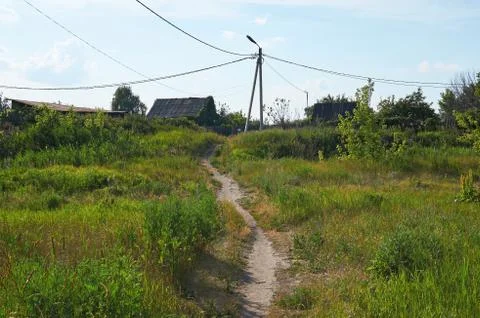A path through a field with green grass to an old village. Stock Photos