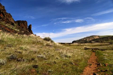 A path through a grassy high desert landscape with distant cliffs and blue sky Stock Photos