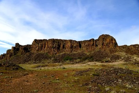 A path through a grassy high desert landscape with distant cliffs and blue sky Stock Photos