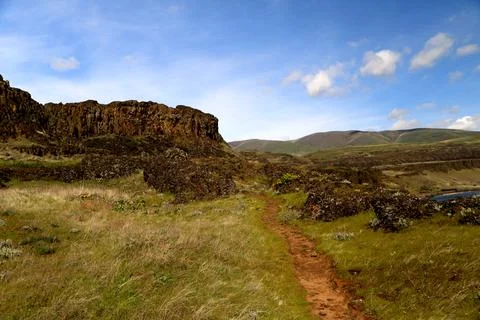 A path through a grassy high desert landscape with distant cliffs and blue sky Stock Photos