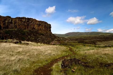 A path through a grassy high desert landscape with distant cliffs and blue sky Stock Photos