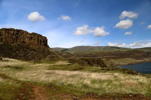 A path through a grassy high desert landscape with distant cliffs and blue sky Stock Photos