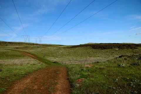 A path through green grassy hills with power lines, a blue sky, and pylons Stock Photos