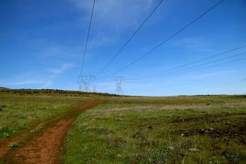 A path through green grassy hills with power lines, a blue sky, and pylons Stock Photos