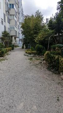 A path of white small stone through a mini park near tall houses Stock Photos