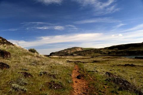 A path winding through a grassy high desert landscape with hills in the distance Stock Photos
