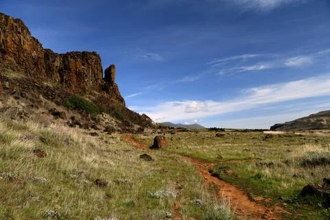 A path winding through a grassy high desert landscape with cliffs and a blue sky Stock Photos