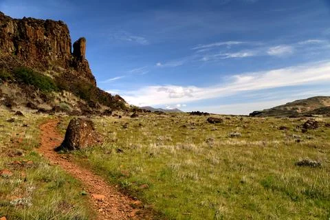 A path winding through a grassy high desert landscape with cliffs and a blue sky Stock Photos