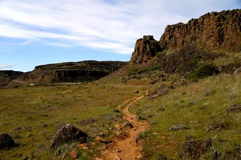 A path winding through a grassy high desert landscape with cliffs  Stock Photos