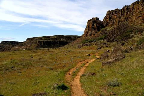 A path winding through a grassy high desert landscape with cliffs  Stock Photos