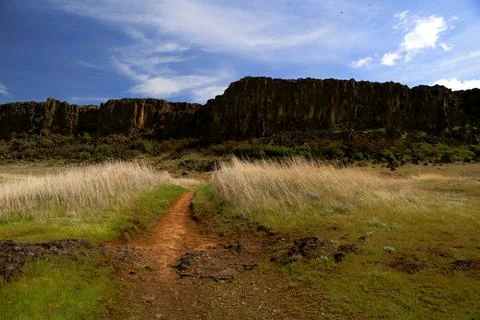 A path winding through a grassy high desert landscape with cliffs and blue sky Stock Photos