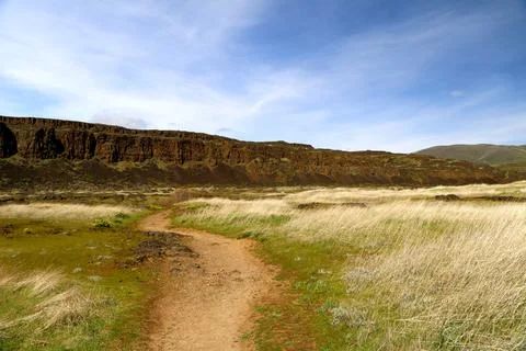 A path winding through a grassy high desert landscape with cliffs and blue sky Stock Photos
