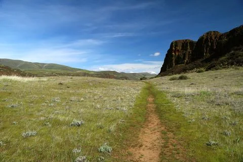 A path winding through a grassy high desert landscape with cliffs and blue sky Stock Photos