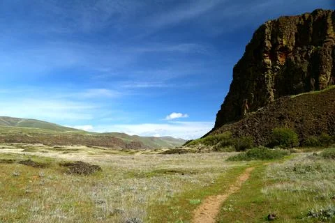 A path winding through a grassy high desert landscape with cliffs and a blue sky Stock Photos