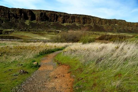 A path winding through a grassy high desert landscape with cliffs and blue sky Stock Photos