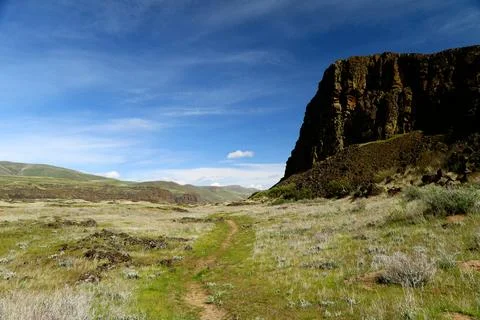 A path winding through a grassy high desert landscape with cliffs and blue sky Stock Photos