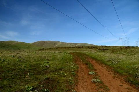 A path winding through green grassy hills with power lines in a blue sky Stock Photos