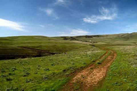 A path winding through green grassy hills with a blue sky above Stock Photos