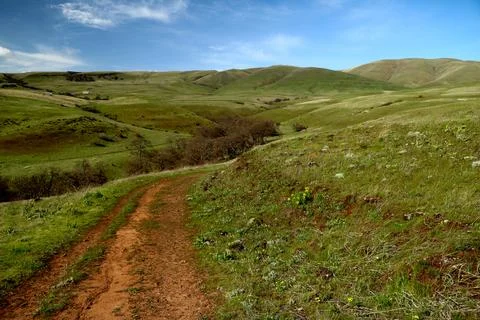 A path winding through green grassy hills with a blue sky above Stock Photos
