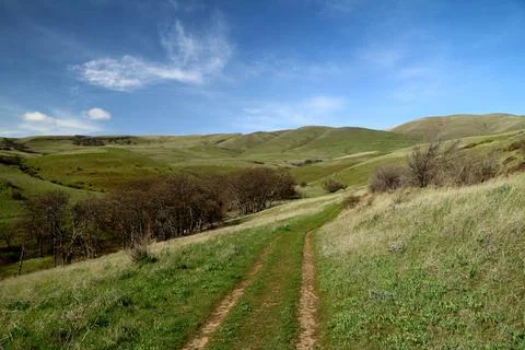 A path winding through green grassy hills with a blue sky above Stock Photos