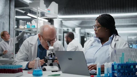 Pathologist examining biopsy slide while coworker documents findings on laptop Stock Footage 325682088
