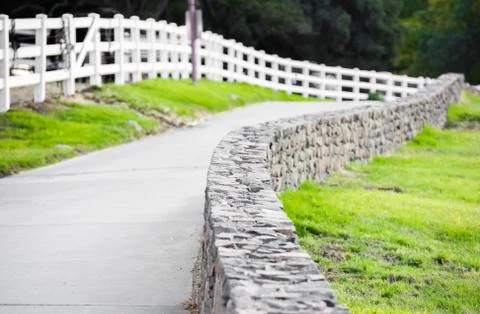 Pathway along a stone wall and a wooden fence Stock Photos