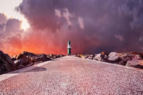 Pathway to Lighthouse on the sea under dramatic fire sky Stock Photos