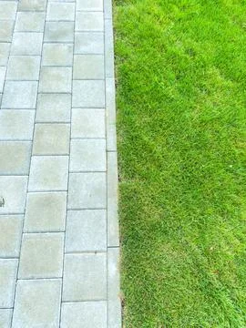 A pathway made of square stones runs alongside a green grassy field. Grass me Stock Photos