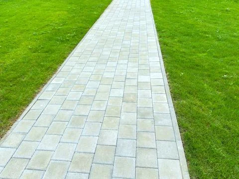 A pathway is made of stone blocks leading through green grass in a public par Stock Photos