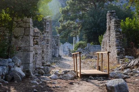 Pathway Through Ancient Olympos Ruins Highlighting Stone Walls and Wooden Bridge Foto stock