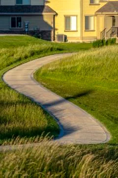 Pathway that winds through a grassy terrain with houses in the background Stock-Fotos