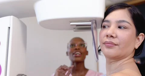 Patient and pink-scrub tech guiding pose and adjusting paddle in clinic for Stock Footage 339414588