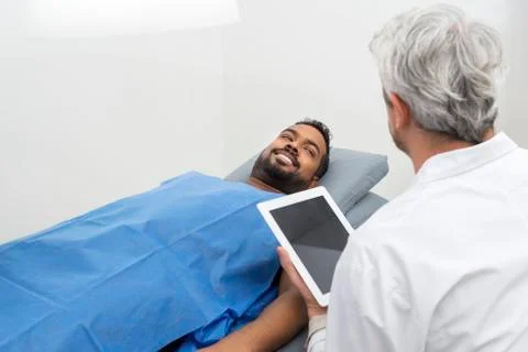 Patient On Bed Looking At Doctor Using Digital Tablet 写真素材