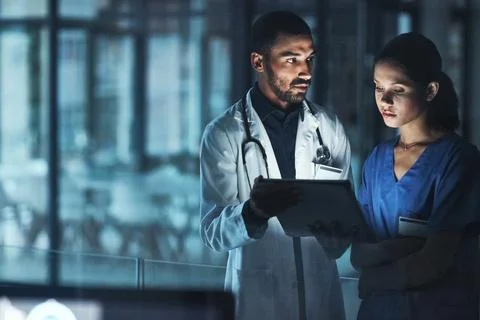 Patient care is a 247 commitment. two young doctors using a digital tablet late Stock Photos