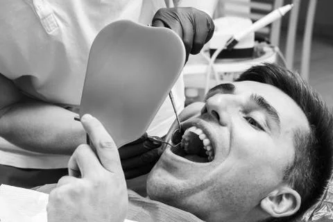 The patient at the dentist,a man holds a mirror in his hands, assesses the co Stock Photos