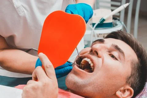 The patient at the dentist,a man holds a mirror in his hands, assesses the co Stock Photos