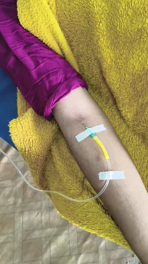 Patient Hand with IV Drip Bottle Attached in Hospital Scene Видео 320387141