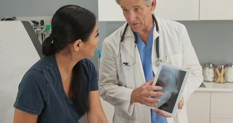 Patient looking at tablet computer with knee x-ray as doctor explains injury Stock Footage 101398497