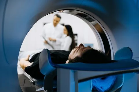 Patient lying on CT scanner table, surrounded by medical professionals disc.. Stock Photos