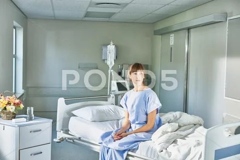 Patient Sitting On Hospital Bed Wearing Hospital Gown