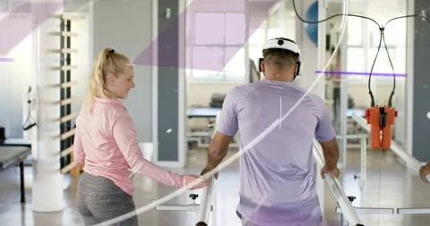 Patient stepping between parallel bars in rehab gym therapist supporting wrist Stock-Footage 316605539